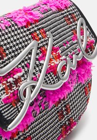 Borsa in tessuto testurizzato bianco e nero con accenti rosa e rossi. Presenta un logo metallico argento "Haul" sulla parte superiore. Forma arrotondata.