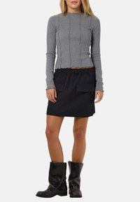 Haut gris à manches longues côtelé avec des coutures décoratives, associé à une jupe noire à rayures fines dotée de grandes poches, et des bottes noires texturées montantes.