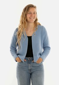 Lichtblauwe gebreide cardigan met een textuur afwerking, open voorkant en lange mouwen. Gepaard met hoge taille spijkerbroek.