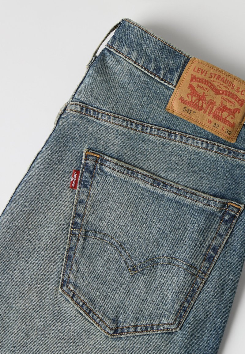 Blå Levi's jeans i denim foldet, så baglommen med signaturbroderi og brun lædermærke på linningen vises.