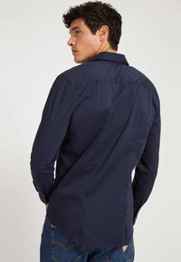 Camisa de manga larga azul marino con cuello abotonado, hecha de tela suave, con un corte ajustado y un dobladillo curvo.