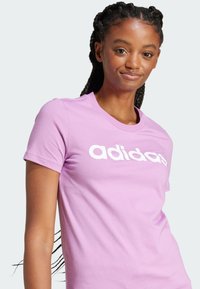 Jasnofioletowy bawełniany t-shirt z białym logo "adidas" na klatce piersiowej, krótkie rękawy i okrągły dekolt. Miękka struktura.