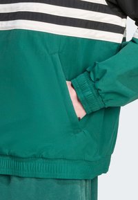 Roheline kruviga jakki musta ja valge triibuline disain. Omab elastseid mansette ja küljetaskut. Sujuv, kerge kangas.