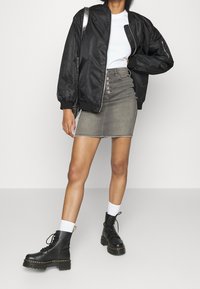 Chaqueta bomber negra con puños acanalados, camiseta blanca, falda de mezclilla gris con detalle de botones y botines negros de cordones con suelas gruesas.