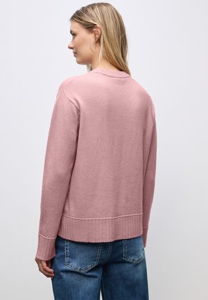 Rosa gestrickter Pullover mit geripptem Saum und Ärmelbündchen, runder Ausschnitt und lockerer Passform. Getragen mit blauen Jeans.