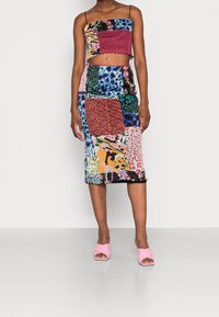 Lappat tvådelat set med en kort topp med tunna axelband och en midikjol. Färgerna inkluderar rosa, blå, grön och djurmönster. Rosa klackar.