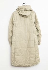 Beige lång kviltad vinterjacka med huva, synlig sömnad och en liten etikett nära nederkanten mot en vit bakgrund.