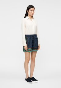 Camisola branca de manga comprida usada com calções azul-marinho com bolinhas brancas e detalhes coloridos com padrões. Par de ténis escuros completa o conjunto.