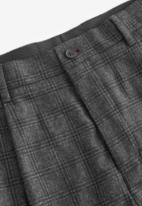 Pantalons à carreaux gris en tissu texturé, dotés d'une fermeture à bouton et d'une doublure intérieure lisse. Détail de motif écossais visible.