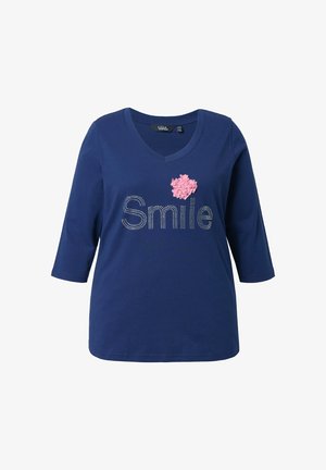 Námořnická modrá trička s výstřihem do V a tříčtvrtečními rukávy. Nápis "Úsměv" z kamínků a růžový texturovaný květinový akcent na levé straně hrudi.