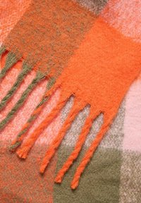 Nærbillede af bløde uldsjaals frynser i orange, pink og olivengrøn rutemønster med snoede kvaster.