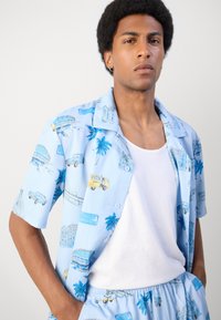 Chemise à manches courtes, à boutons, en tissu bleu clair, ornée d'imprimés tropicaux de voitures, de palmiers et de points d'intérêt dans des couleurs contrastées.