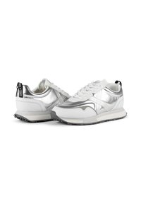 Baskets blanches avec des accents métalliques argentés, présentant un dessus texturé, un design à lacets et un onglet de talon noir contrastant.