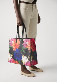 Bloemen totebag met levendige roze, blauwe en witte bloemen op een zwarte achtergrond; stevige zwarte handvatten; geometrische vorm; BAKER LONDON branding.