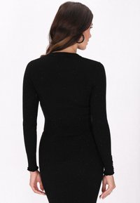 Top negru cu maneci lungi, cu un design ajustat. Materialul texturat prezintă sclipiri subtile. Mansetele volan sunt detalii adăugate la mâneci.