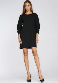 Czarna sukienka z okrągłym dekoltem i rękawami do połowy ramienia. Gładki materiał, lekko luźny krój, sięgająca do połowy uda. Noszona z czarnymi szpilkami.