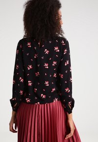Black floral blouse with pink flowers, long sleeves, buttoned cuffs, keyhole back detail, paired with a pleated maroon skirt.