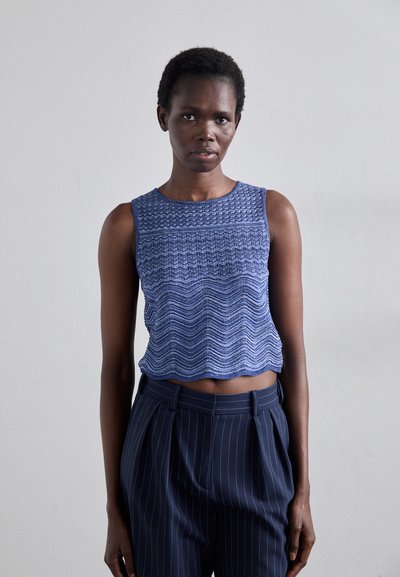 Blue knitted crop top with textured wave pattern, paired with high-waisted navy pinstripe trousers. Smooth fabric, sleeveless design.