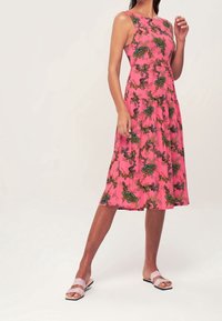 Rosa ärmelloses Kleid mit floralem Muster in Grün- und Dunkelakzenten; knie-lange Ausführung; Model trägt helle Sandalen.