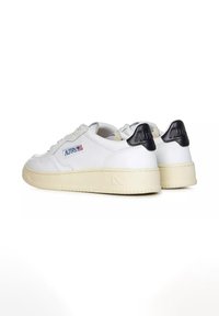 Sneakers bianchi in pelle con accenti neri nel tallone, punta rotonda, design con lacci e suola testurizzata color crema. Presentano un dettaglio del logo sul lato.