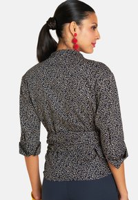 Musterbluse mit dunkelblauem Hintergrund und goldenen Wirbeln. Das Shirt hat aufgerollte Ärmel und ein tailliertes Design.
