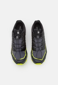 Scarpe da trail running nere e grigie con una parte superiore testurizzata, accenti gialli audaci e un sistema di allacciatura sicuro per un miglior fit e supporto.