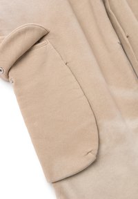 Suéter beige con una textura suave, que presenta un gran bolsillo, cierre de botones en la parte delantera y cuello curvado. El diseño es casual y relajado.