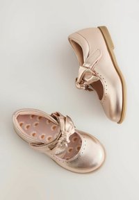 Metallic rosegouden Mary Jane schoenen met een strik en een uitsnijdingsontwerp, voorzien van een patroon op de binnenzool met madeliefjes en een lage bruine zool.