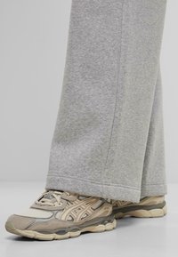 Des chaussures de sport beiges et grises avec des empiècements en maille et texturés, assorties à un pantalon de survêtement gris à jambes larges en tissu doux et chiné.