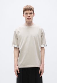 Beiges Baumwoll-T-Shirt mit kurzen Ärmeln und gestreiftem Bündchen. Einfaches Rundhalsausschnitt-Design und entspannte Passform mit glatter Textur.