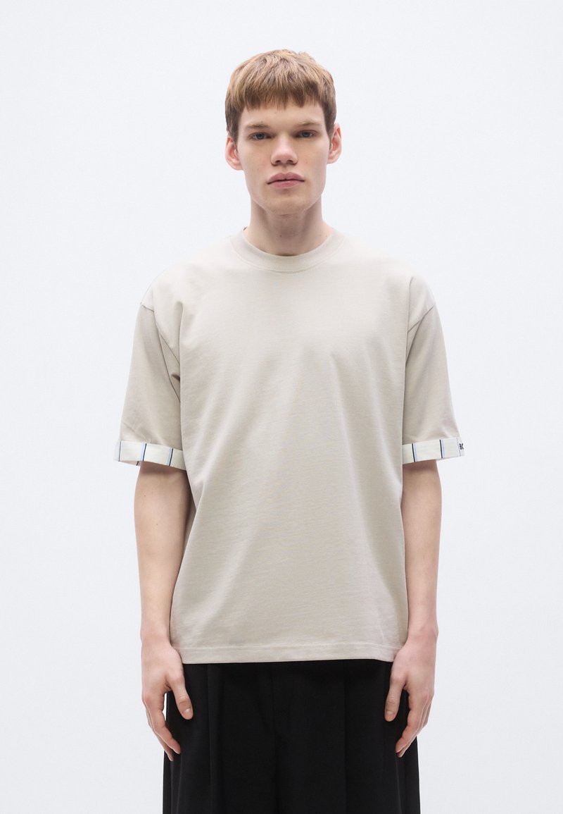 Beiges Baumwoll-T-Shirt mit kurzen Ärmeln und gestreiftem Bündchen. Einfaches Rundhalsausschnitt-Design und entspannte Passform mit glatter Textur.