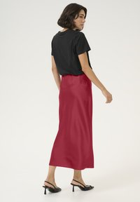 T-shirt noir à manches courtes associé à une longue jupe en satin rouge lisse, longueur cheville, complétée par des sandales à talons noirs.
