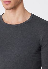 Dunkelgraues Langarmshirt mit rundem Ausschnitt. Der Stoff wirkt glatt und hat einen taillierten Schnitt, der eine subtile Textur zeigt.