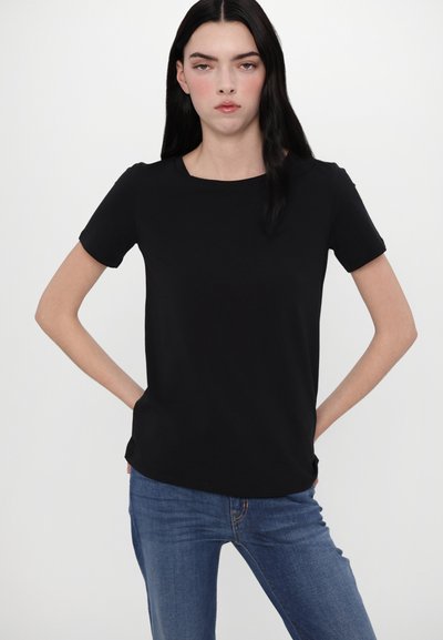 Sort kortærmet top med rund halsudskæring, lavet af et glat stof. Den har en afslappet pasform og er parret med blå jeans.