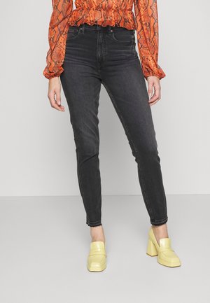 Jeans pretos de cintura alta com um corte justo e bainha bruta. Combinados com sapatos de salto bloco amarelos brilhantes. Blusa com estampado de cobra laranja.