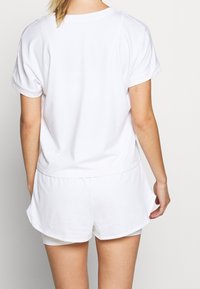 Top blanco de manga corta con dobladillos enrollados, combinado con pantalones cortos blancos. La tela parece suave con una textura sutil.