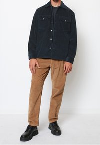 Granatowa kurtka koszulowa z sztruksu z dwoma kieszeniami na piersi, zapinana na guziki, w zestawie z jasnobrązowymi spodniami ze sztruksu i czarnymi sznurowanymi butami.