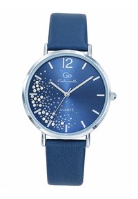 Montre à quartz avec un cadran bleu, des accents argentés et un bracelet en cuir bleu texturé. Présente des embellissements en cristal et des index horaires audacieux.
