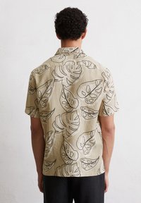Kurzarmhemd aus lichtbeige Leinen mit einem schwarzen Blättermuster. Lockerer Schnitt mit Kragen und geradem Saum.