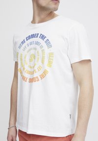 Weißes Baumwoll-T-Shirt mit buntem kreisförmigem Textdruck und Sprüchen. Kurze Ärmel, Standardpassform und ein kleines Markenlabel an der Seite.