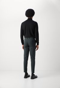 Zwarte lange mouwen turtleneck gecombineerd met donkergroene slim-fit broeken en zwarte schoenen. Gladde stof, op maat gemaakte pasvorm en subtiele details zichtbaar.