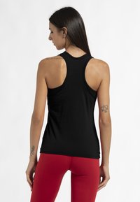 Zwarte racerback tanktop van gladde stof, met een aansluitend ontwerp en zijnaad. In combinatie met rode leggings, wat een strakke silhouet benadrukt.