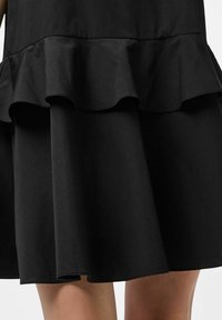 Must mustriga, millel on laienev äär koos volangakujuliste aktsentidega. Valmistatud siledast kangast, sellel on puhas siluett ja pehme, tekstuuriga beleg.