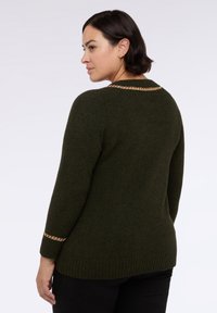 Tmavě zelený pletený svetr s žebrovaným lemem a manžetami, zdobený zlatým řetízkem podél výstřihu a na loktech. Měkká textura.