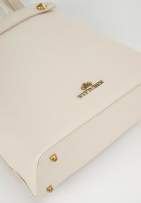 Sac à main en cuir synthétique beige avec des accents dorés, arborant un logo et des clous décoratifs, forme structurée et texture lisse.