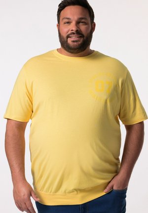 Gelbes T-Shirt mit kurzen Ärmeln und Rundhalsausschnitt sowie einem subtilen Druck "Special Edition 07" auf der Vorderseite. Weicher, struktureller Stoff.