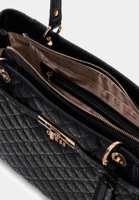 Borsa a tracolla sintetica nera trapuntata con hardware dorato, scomparti con zip e dettaglio del logo. L'interno presenta una morbida fodera beige e stampe del marchio.