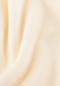 Lichtbeige stof met een gladde textuur en lichte rek, die subtiele ribbeling en zachte draping in fijne plooien toont.