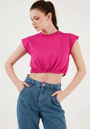 Top corto fucsia con maniche corte, orlo con coulisse elastica e texture liscia. Abbinato a pantaloni in denim blu a vita alta.