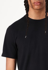 T-shirt de algodão preta com gola redonda e mangas curtas, apresentando uma textura suave. Close-up da área do ombro e do decote visível.